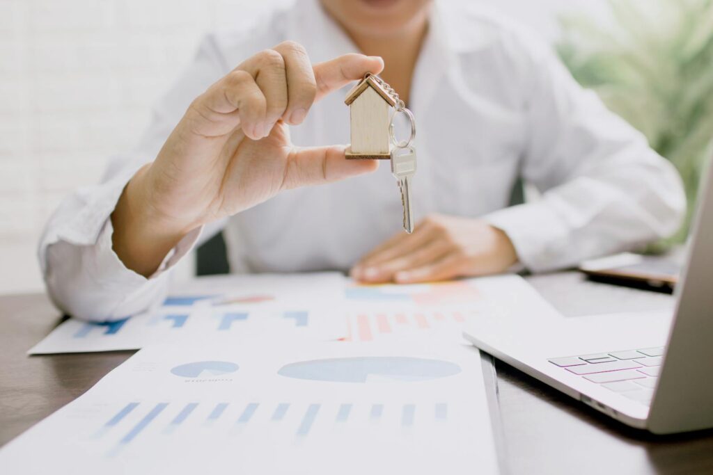 Professionnel de l'immobilier présentant une maquette de maison avec clés, symbolisant l'investissement immobilier et la propriété.